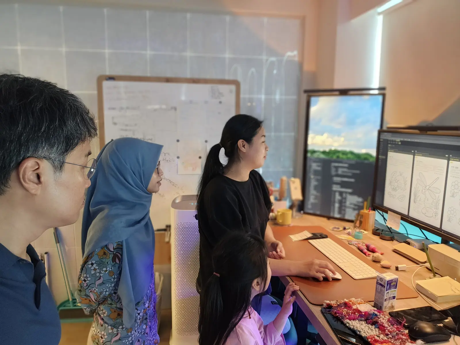Tiga orang kru dan seorang anak bersama-sama melihat tiga sketsa gambar mewarnai di layar monitor.