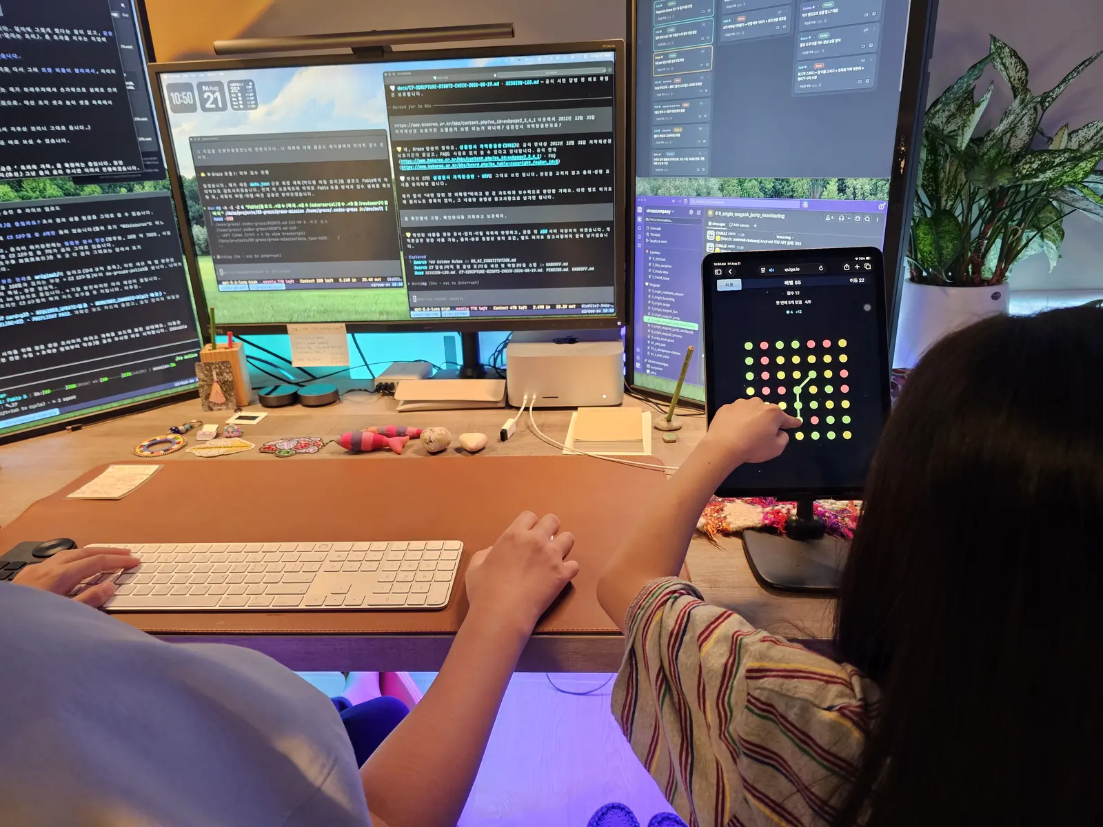 Seorang anak bermain permainan menghubungkan titik di tablet yang berdiri di atas penyangga, sementara di sampingnya orang dewasa bekerja.